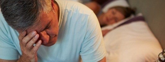 man sitting on edge of bed holding head