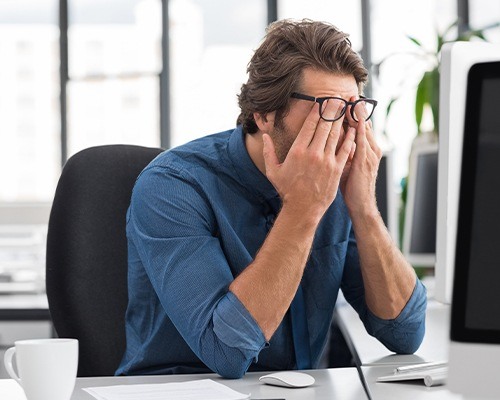 man at desk rubbing eyes