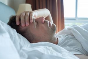 Man lying in bed with a morning headache
