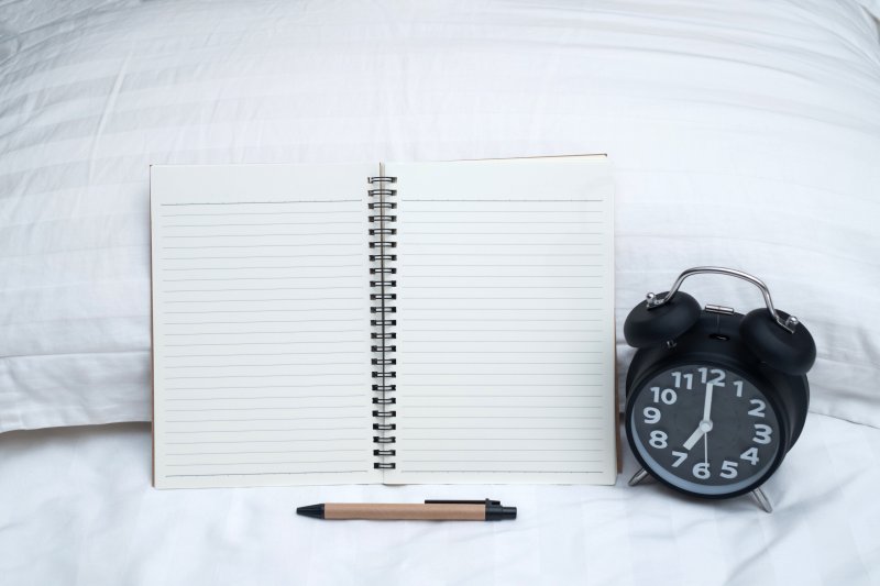 Open notebook on bed with pen and alarm clock