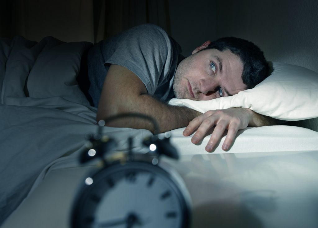 Man wide awake in bed staring at alarm clock