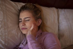 Woman with jaw pain, thinking about visiting dentist for TMJ pain relief