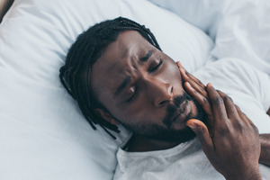 Man with TMJ disorder experiencing jaw pain in bed