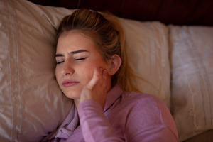 Woman in bed with pain from TMJ disorder