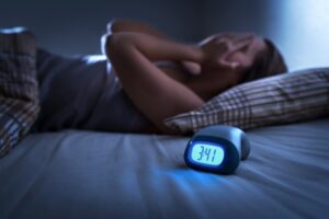 Woman suffering from sleeplessness with clock in foreground.