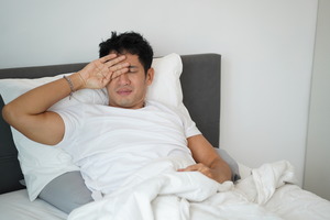 Man in white shirt lying in bed and rubbing his eyes